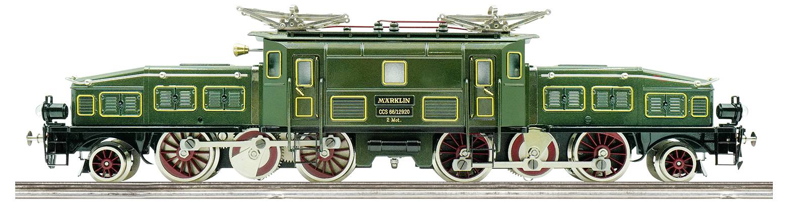 A vintage green model train locomotive with detailed red and black wheels and overhead electrical connectors, viewed from the side.