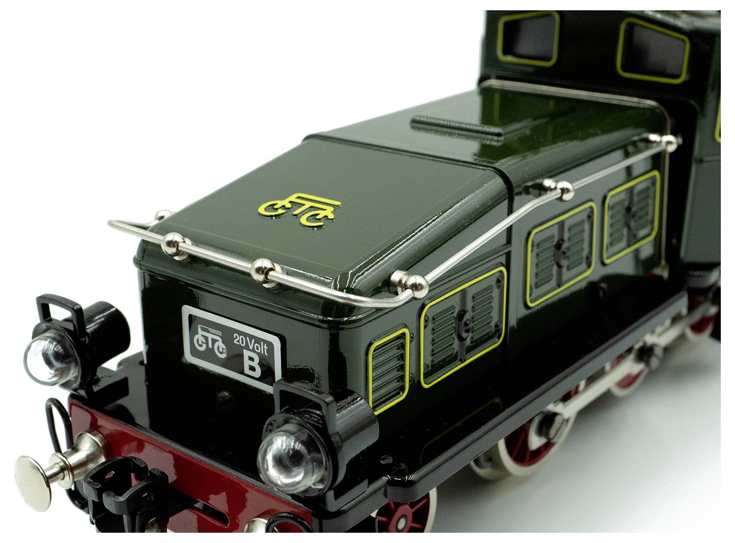 A vintage model train engine in green with black and red details, featuring a yellow logo of a bicycle and '20 Volt B' text on the front.