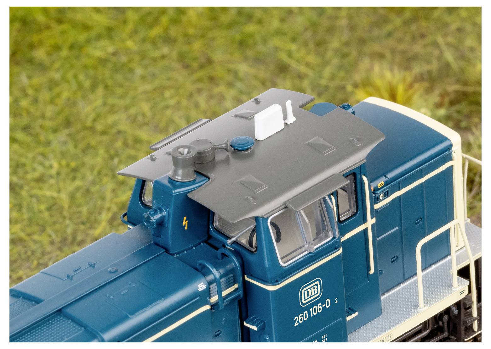 'A detailed miniature model of a blue and gray locomotive with white accents, shown from an elevated perspective against a grassy background.'
