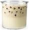 A clear cup filled with creamy, frothy yellow liquid topped with a thicker layer containing brown and black specks.