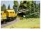 A model railway scene showing a maintenance train with yellow carriages traveling on a curved track beside a forested area and crane equipment.