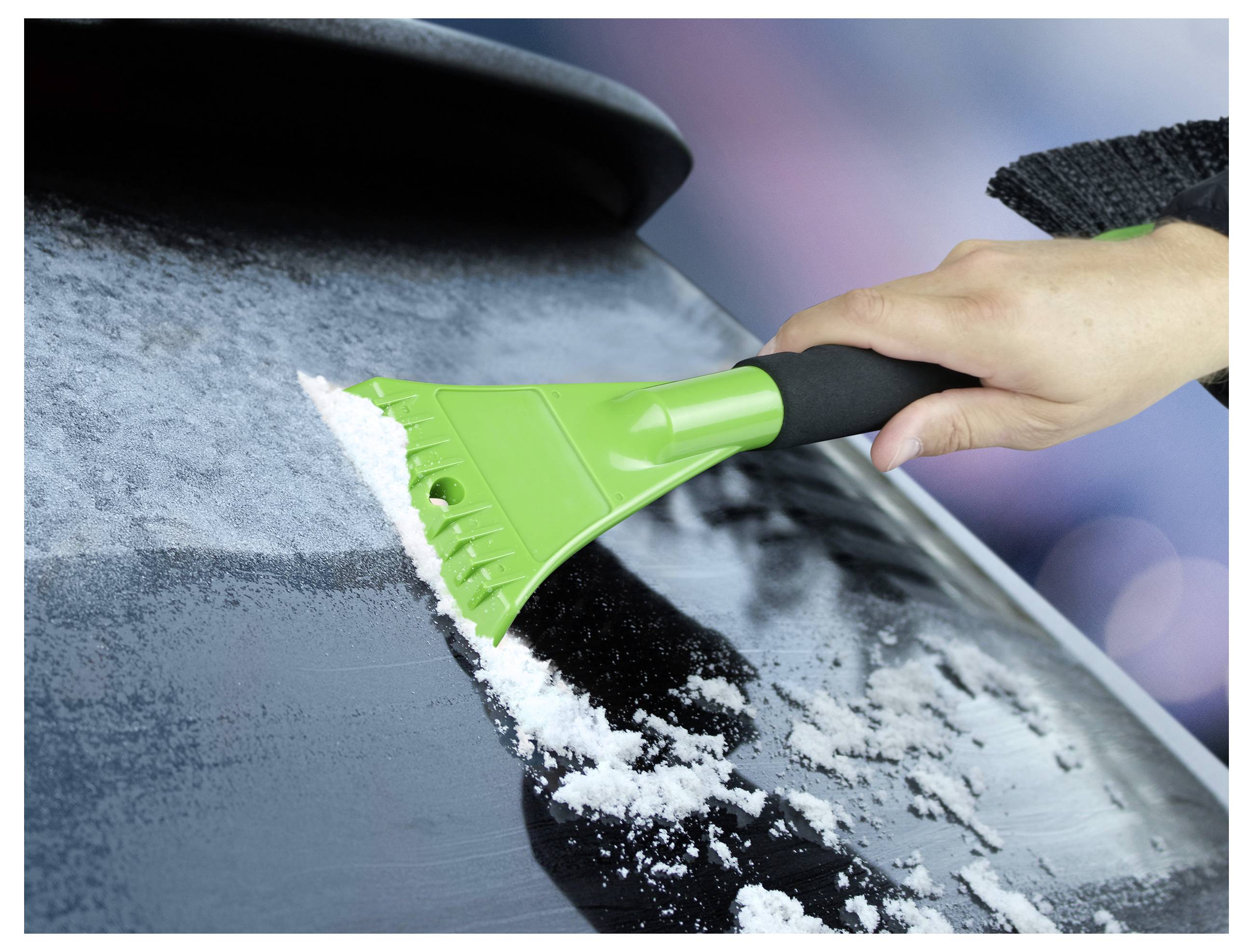 'A hand using a green ice scraper to remove frost from a car window.'