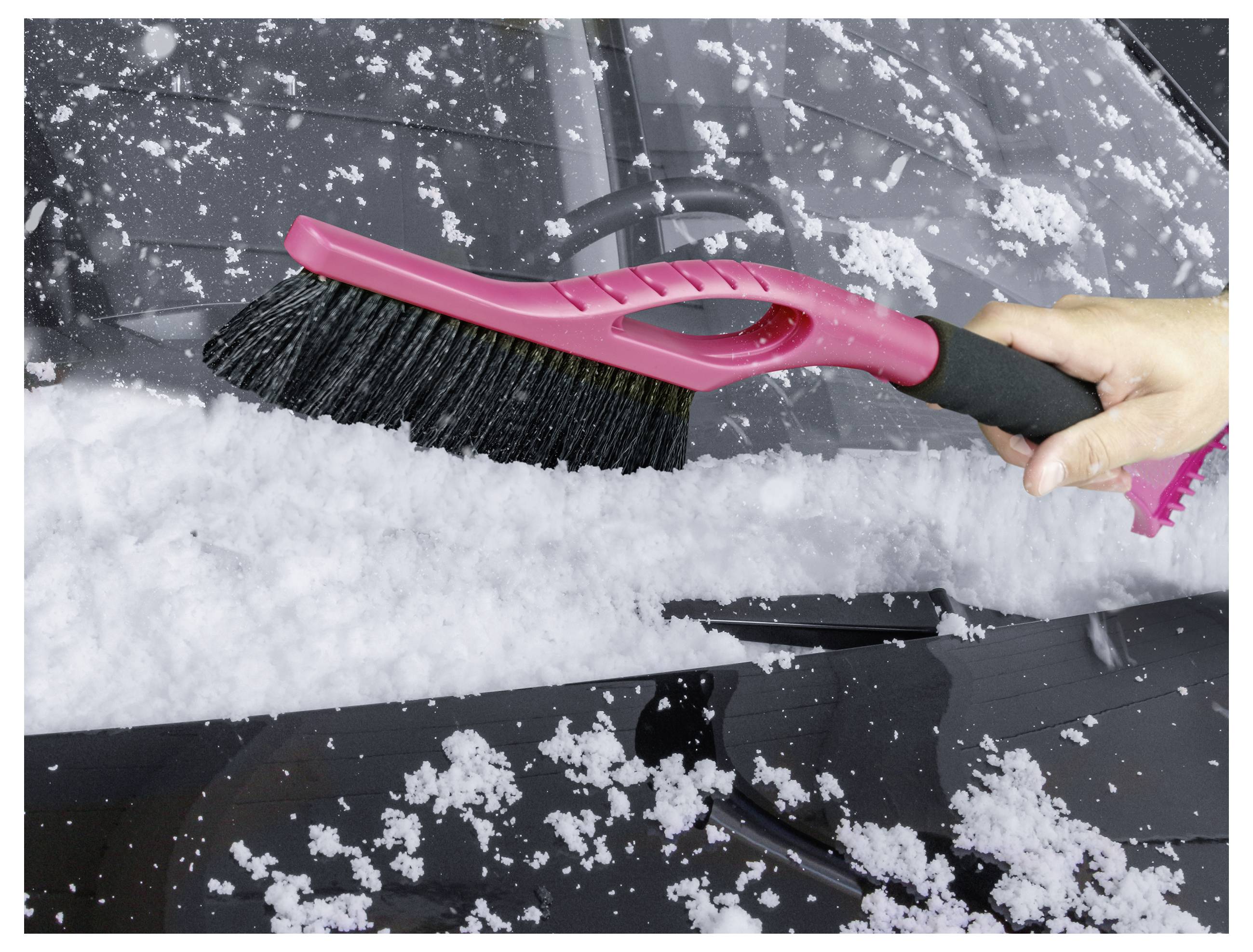 A hand is using a red brush to clear snow from a car windshield.
