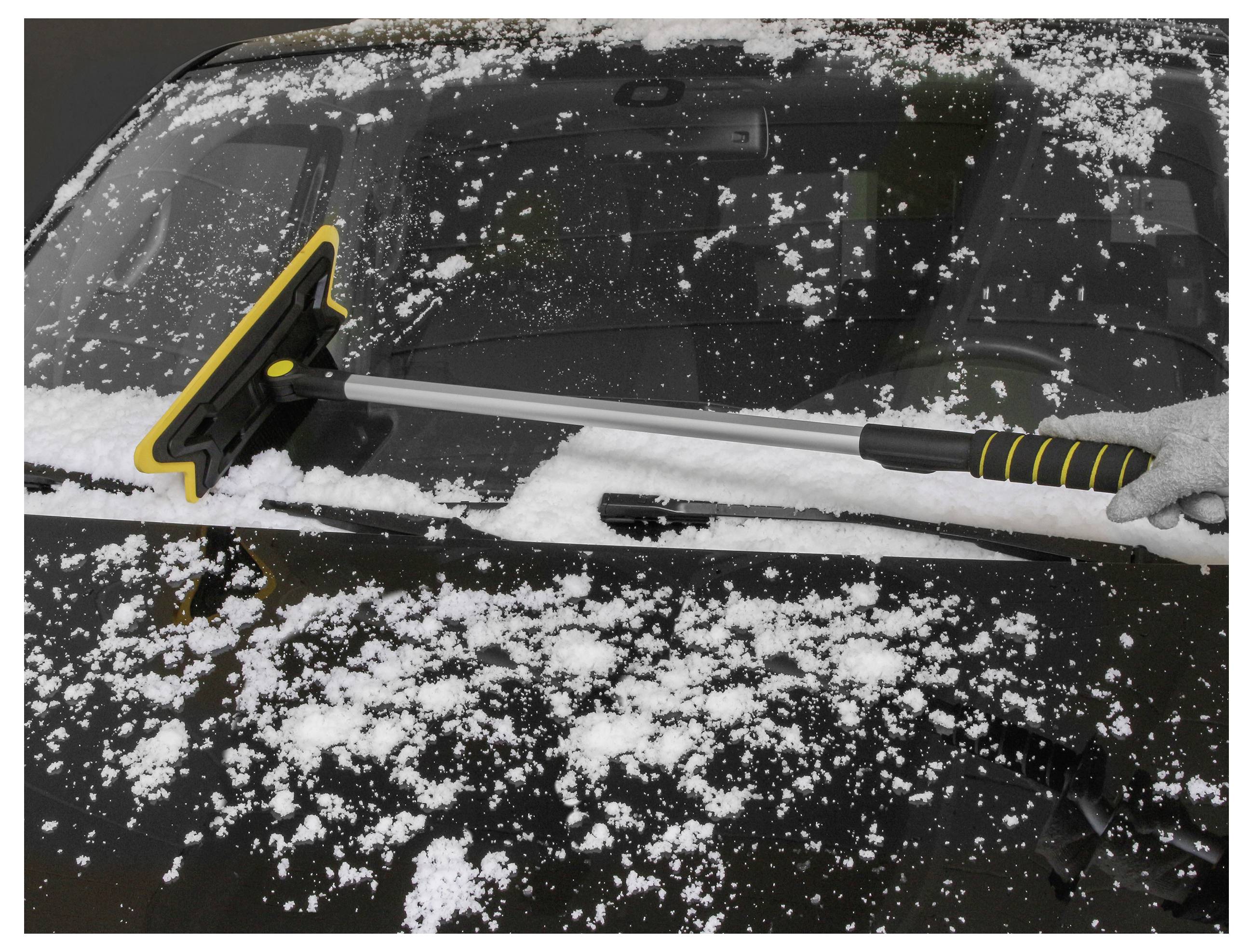 A hand uses a snow brush to clear snow from a car's windshield, showcasing winter weather and vehicle maintenance.
