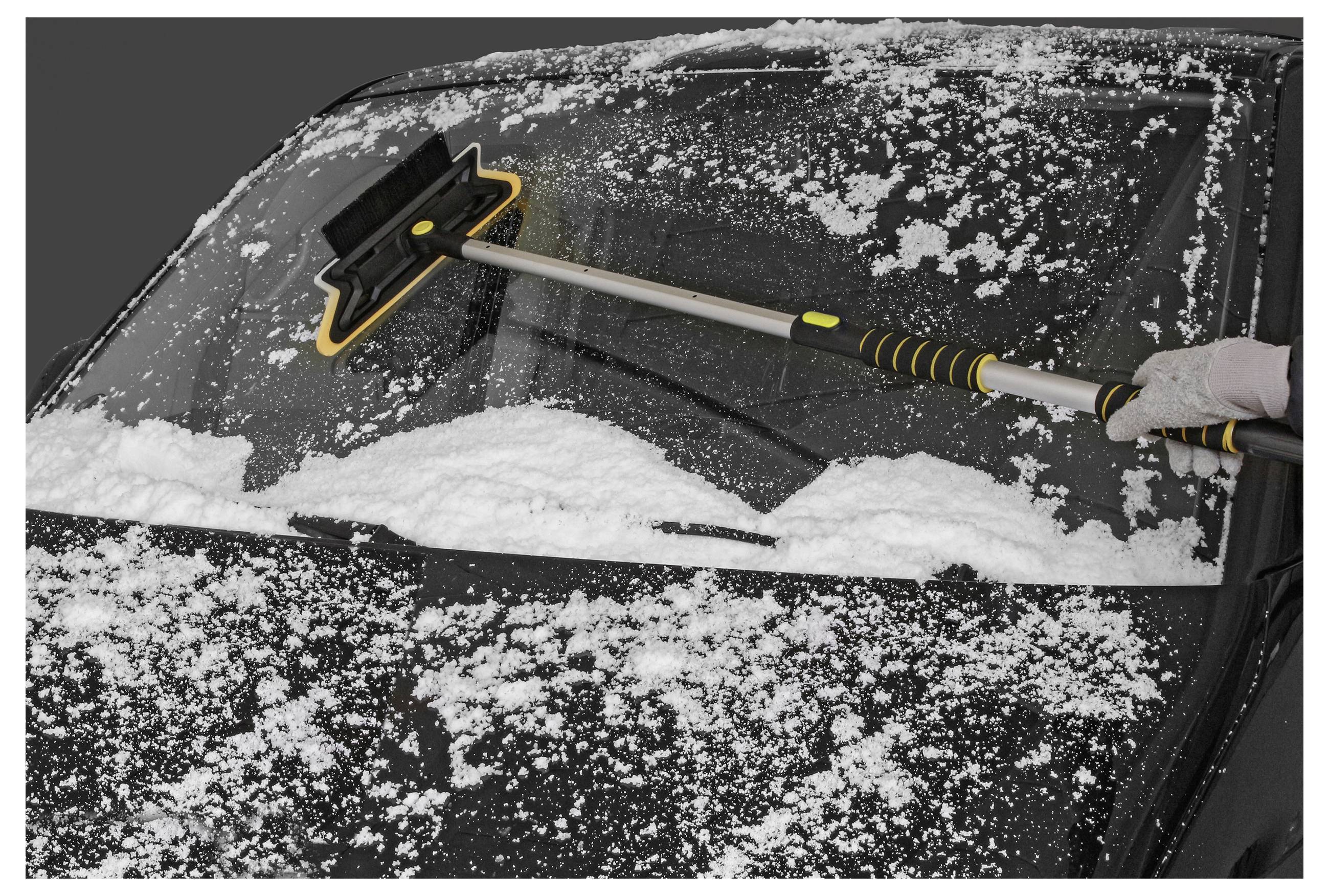 A person uses a snow brush to clear snow from a car windshield on a cold, snowy day.