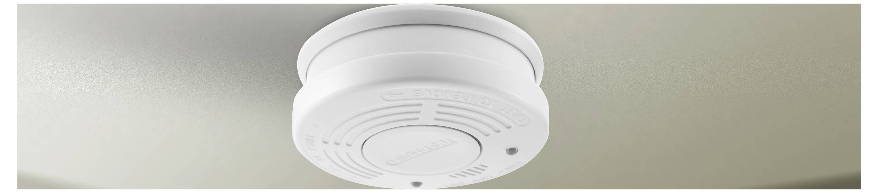 A ceiling-mounted smoke detector with a circular design and ventilation openings is shown from below.