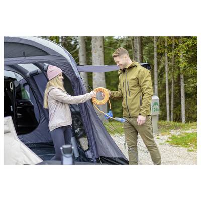 Man and woman at a campsite exchange an orange extension cord beside an open tent in a wooded area.
