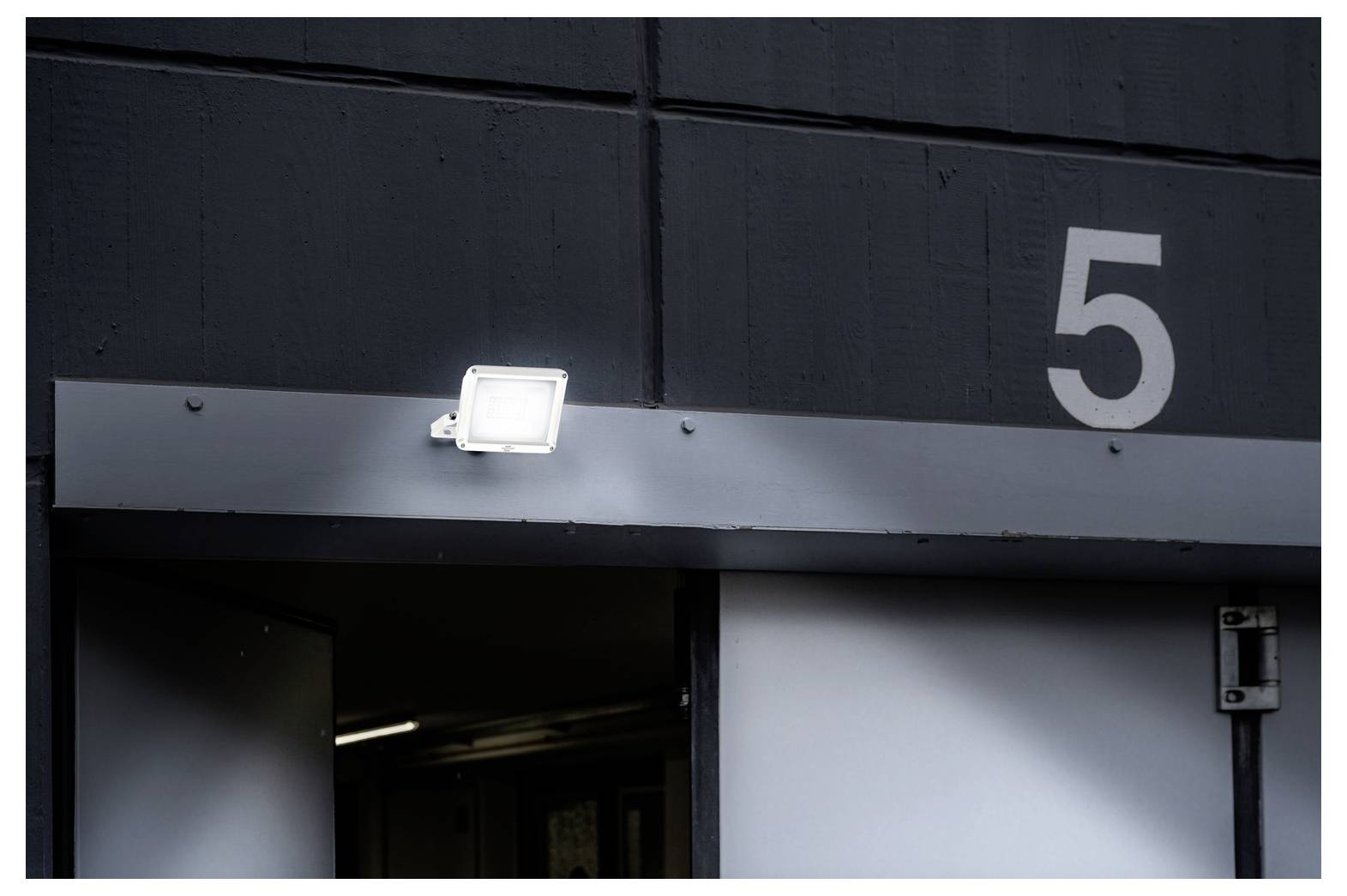 'Number 5' is displayed on a dark wall above an entrance with an open door, illuminated by a bright spotlight.