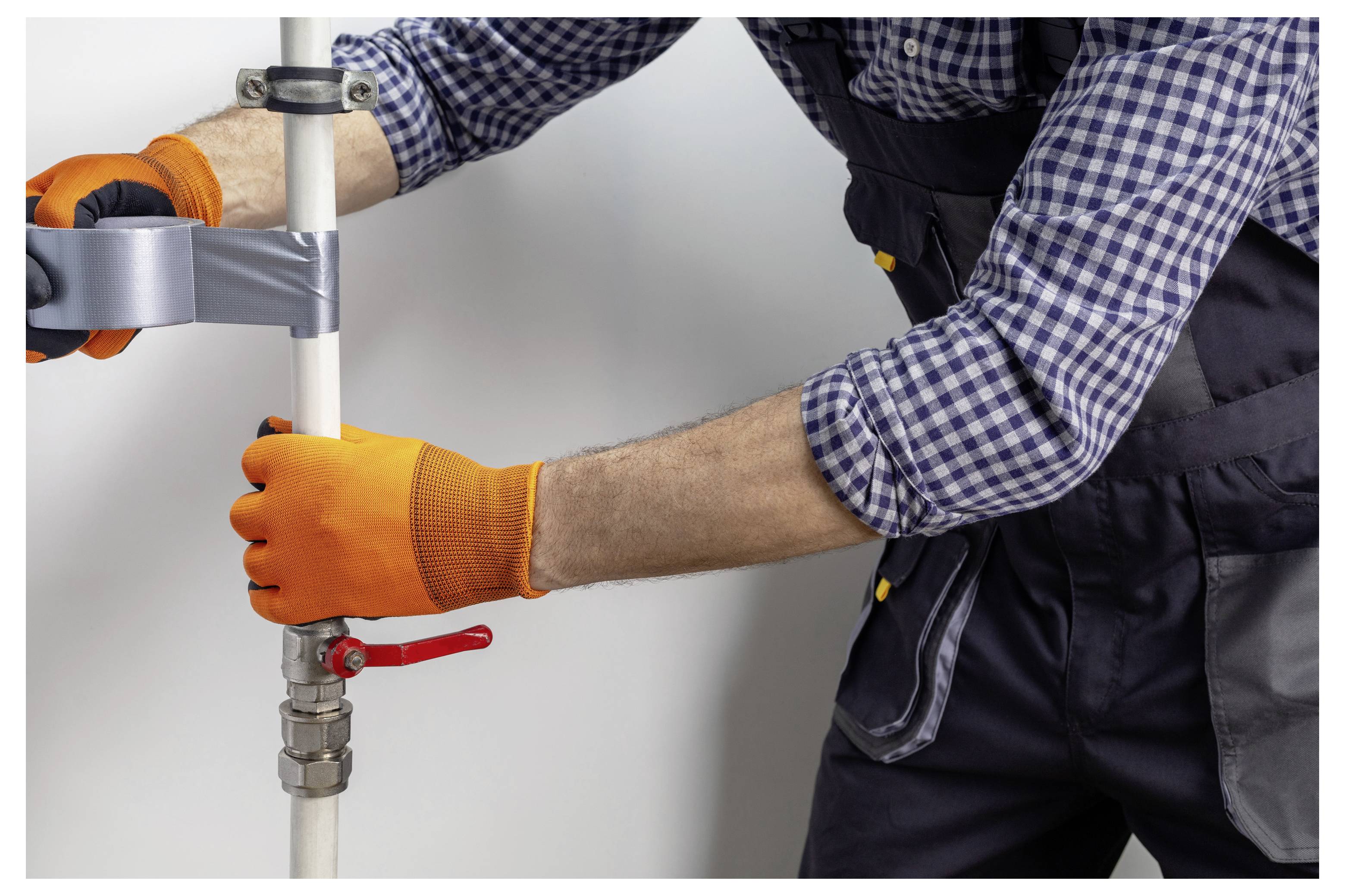 Gloved worker tightening a metal pipe clamp on a vertical white pipe with a wrench, suggesting plumbing installation or repair.