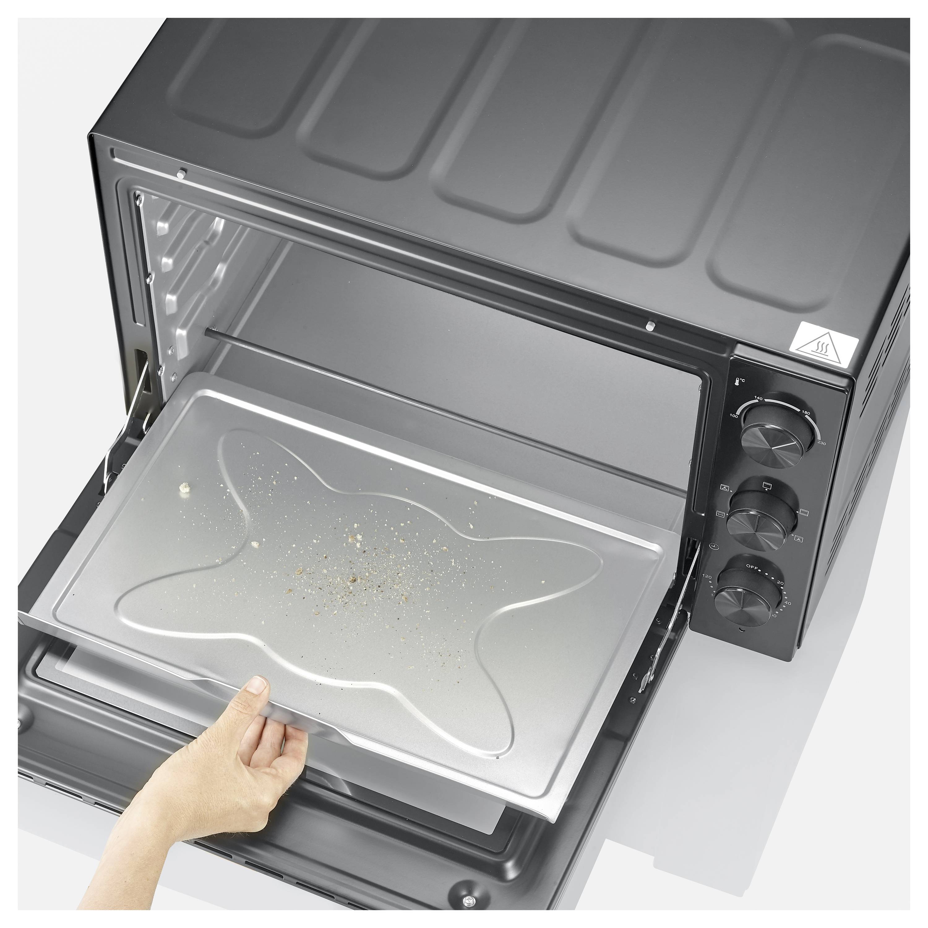 A hand placing a dirty baking tray into an empty, open toaster oven, showing the oven's controls and interior.