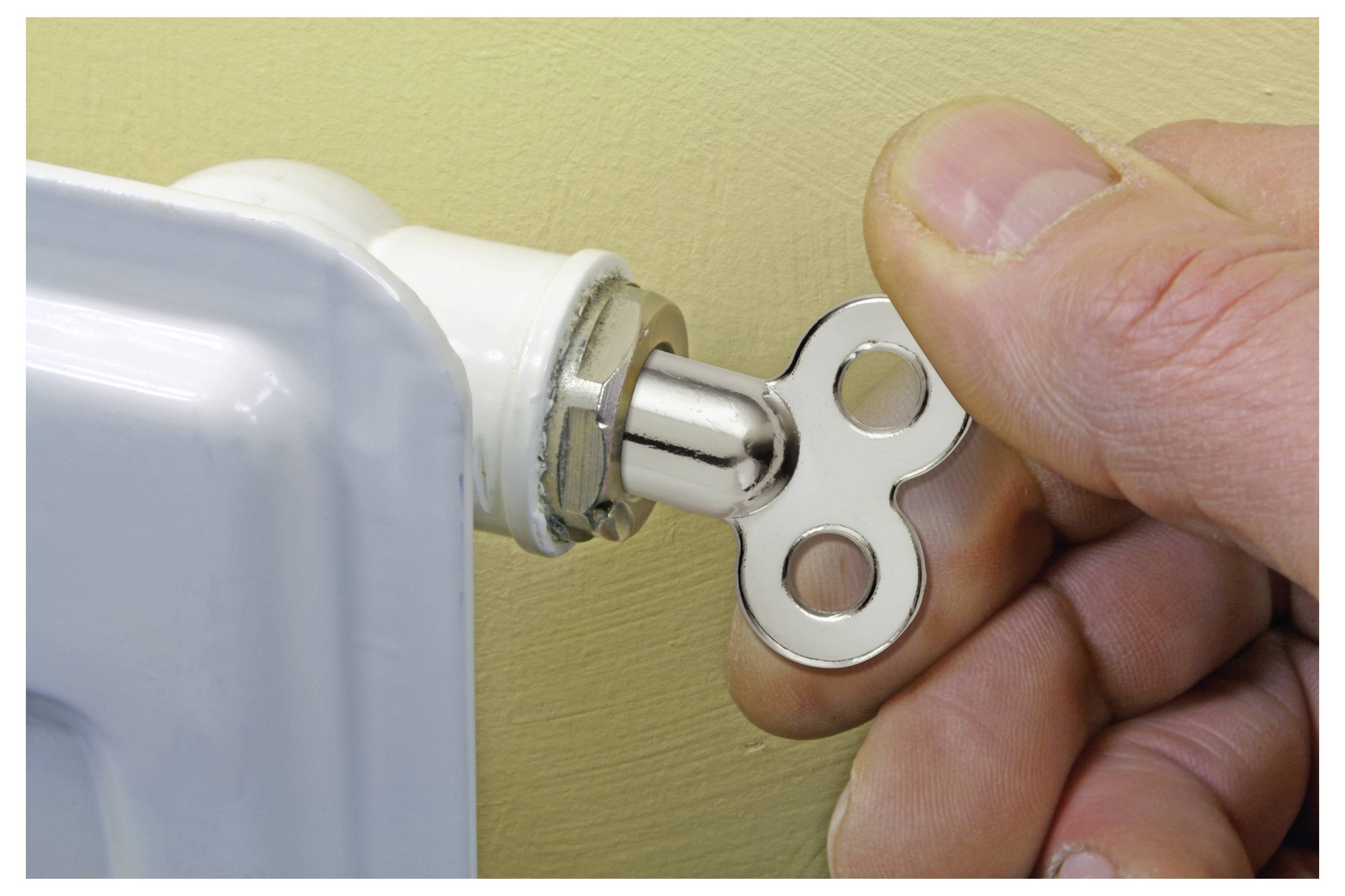 Hand using a key to open or tighten a radiator valve on a metal panel heater.
