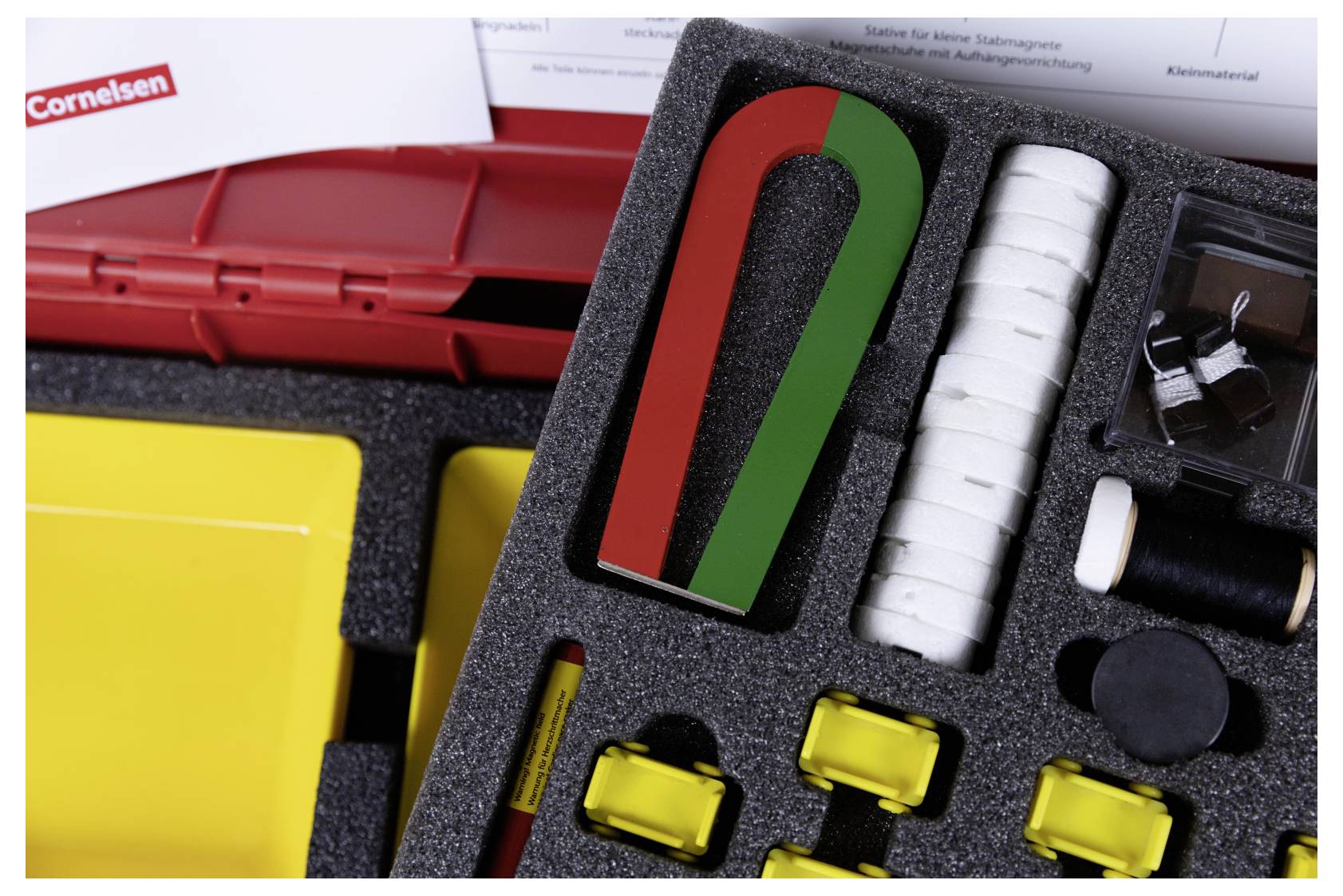 A foam tray containing a red and green horseshoe magnet, white circular pieces, yellow clips, and other small educational tools.