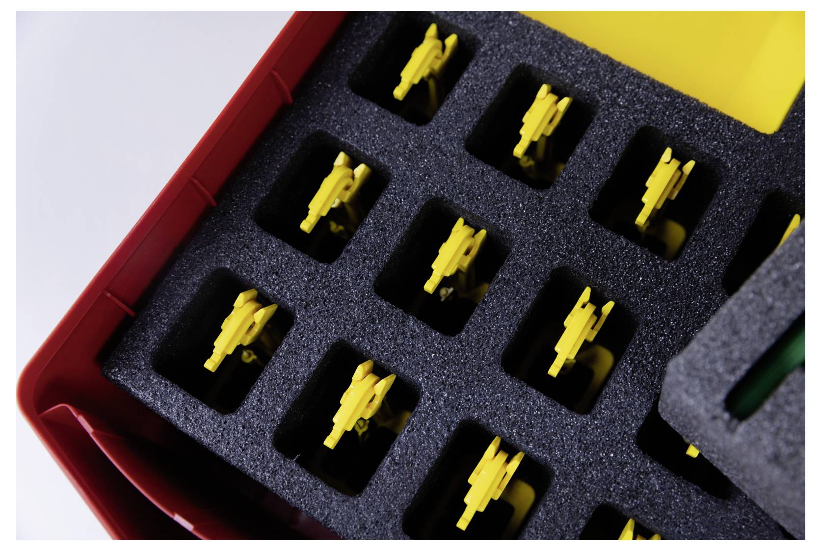 A red container holds yellow plastic components in a black foam organizer with rectangular slots, viewed from above.
