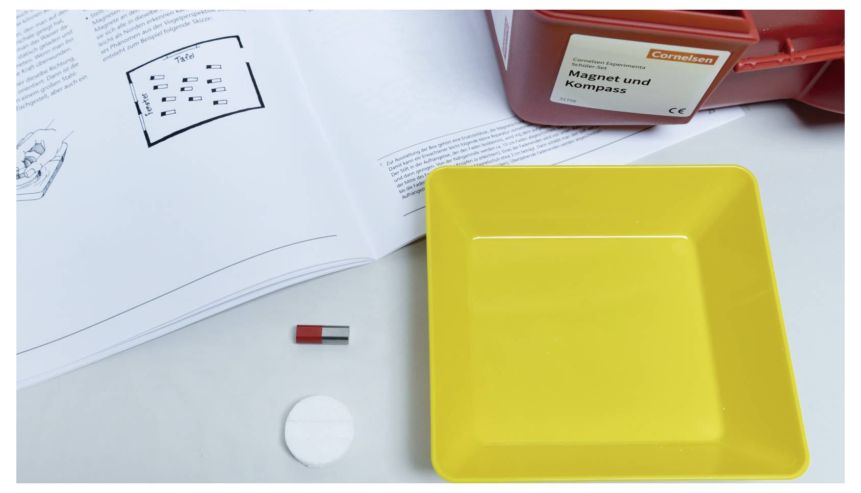 'Magnet und Kompass' kit with magnet and compass on white surface; instructions and yellow tray nearby.