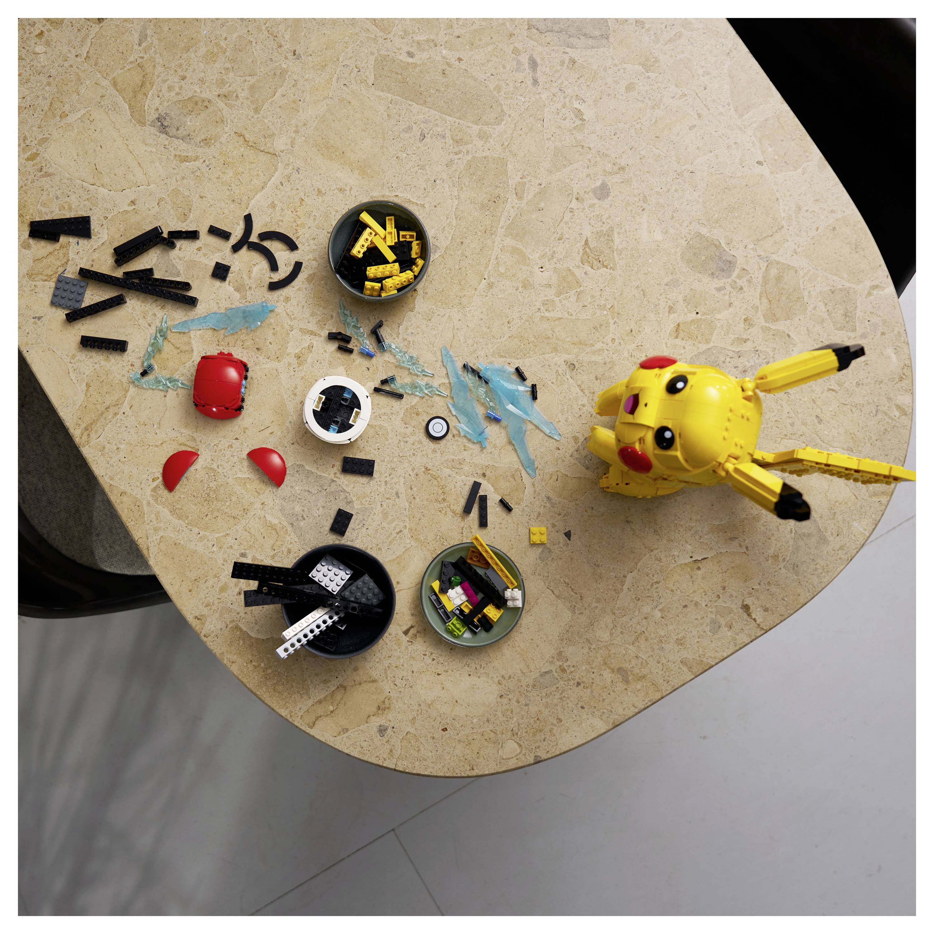A partially assembled yellow toy resembling a fictional character is on a beige table surrounded by various black and red plastic pieces.