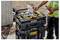 A worker arranges tools in a black and yellow DEWALT storage case, holding a power drill. The setting appears to be a construction site.