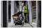 A construction worker in a hard hat and safety vest pulls a stacked tool case on wheels through a narrow hallway on a construction site.