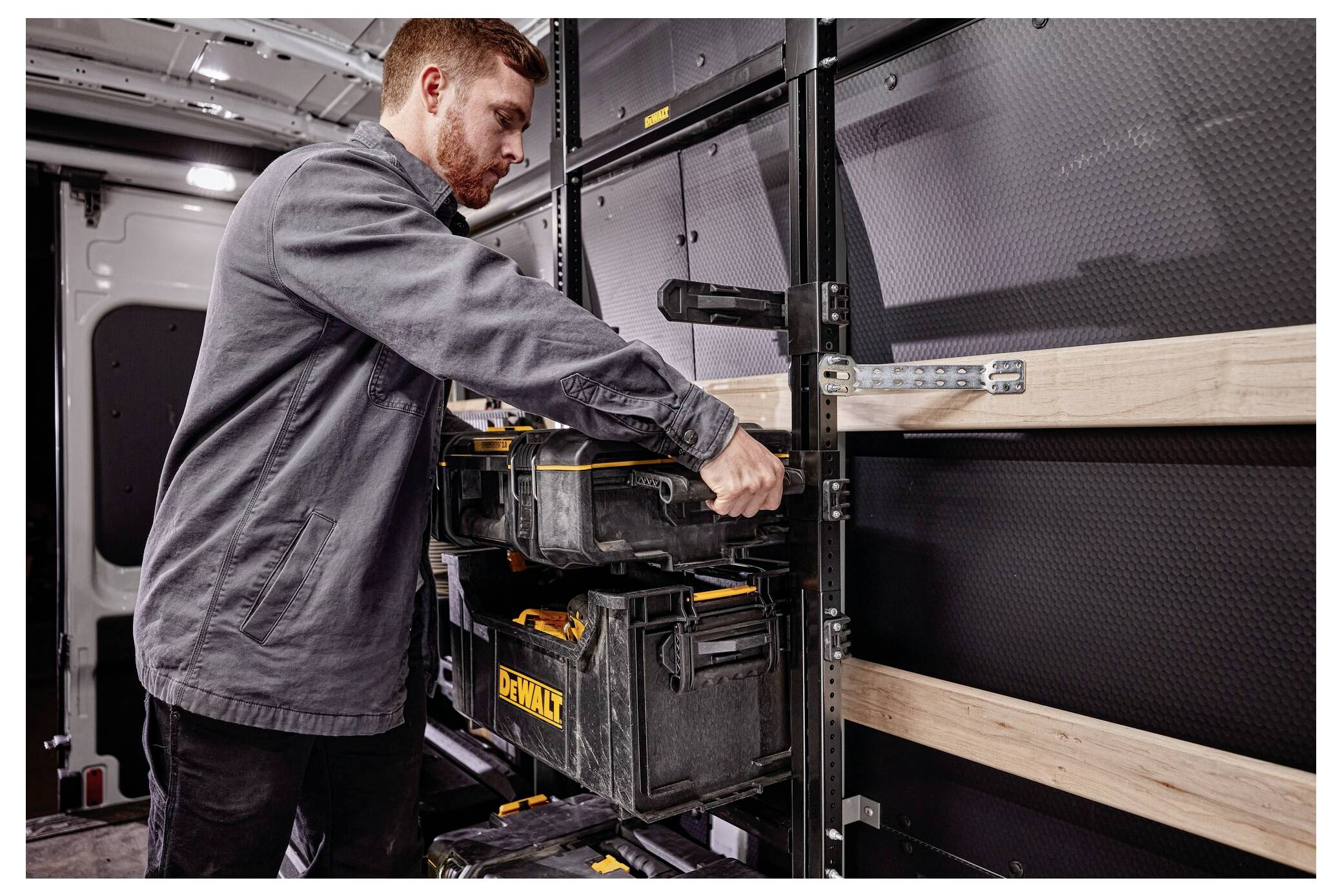 A person organizes toolboxes on shelves inside a vehicle, focusing on storage and organization.