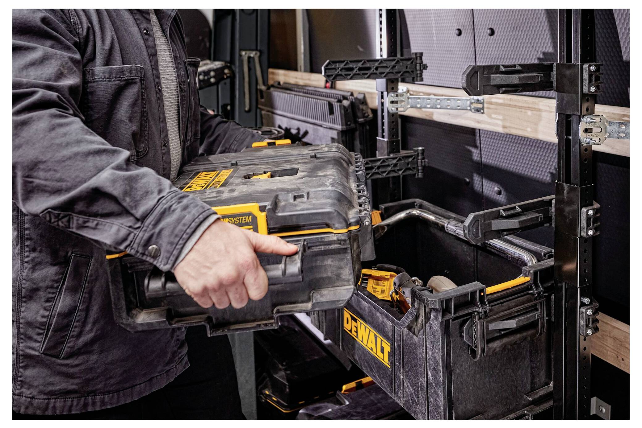 A person placing a black tool case into a van storage system, organized with multiple shelves and tool holders.