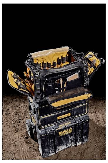 A black and yellow tool bag with various compartments and tools displayed, set atop stacked toolboxes on a dirt surface.