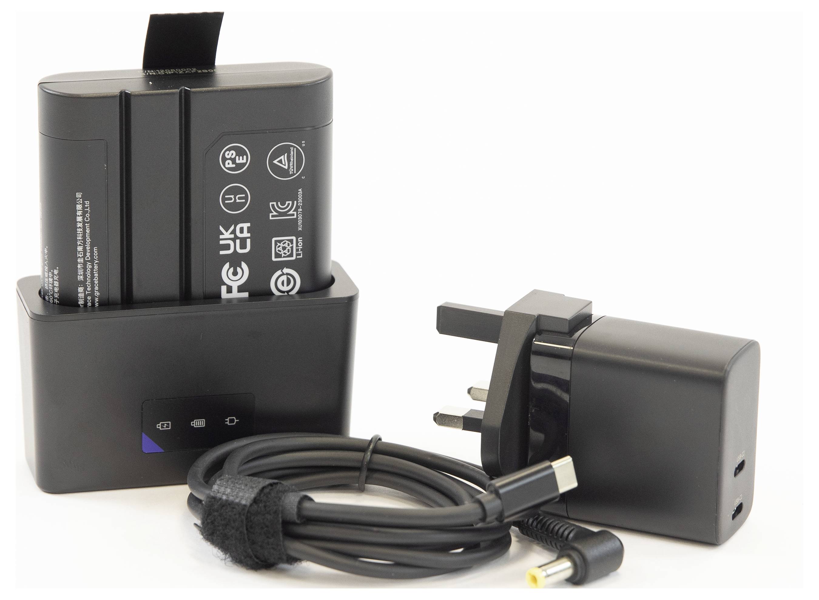 A black battery pack sits upright in a charger dock, accompanied by a power adapter with a UK plug and coiled charging cable.