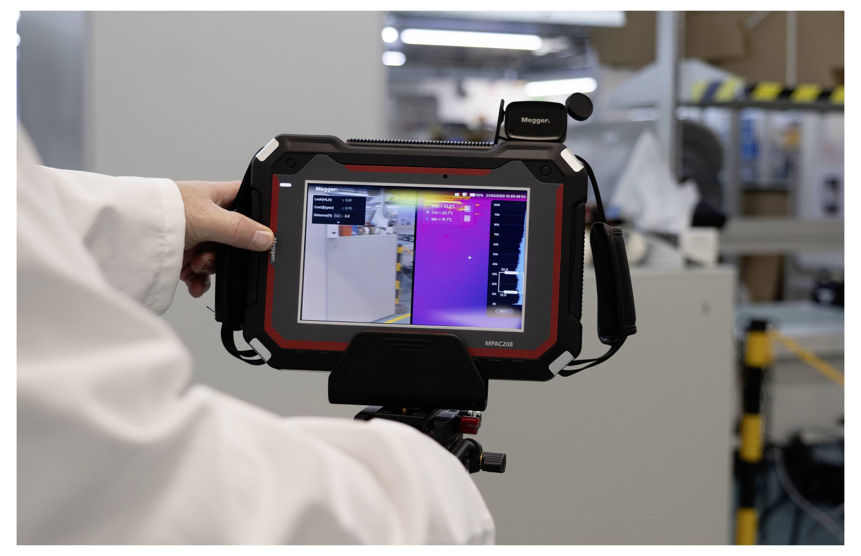 A person in a lab coat holds a thermal imaging device showing a color-coded heat map on the screen, used for monitoring equipment temperature.
