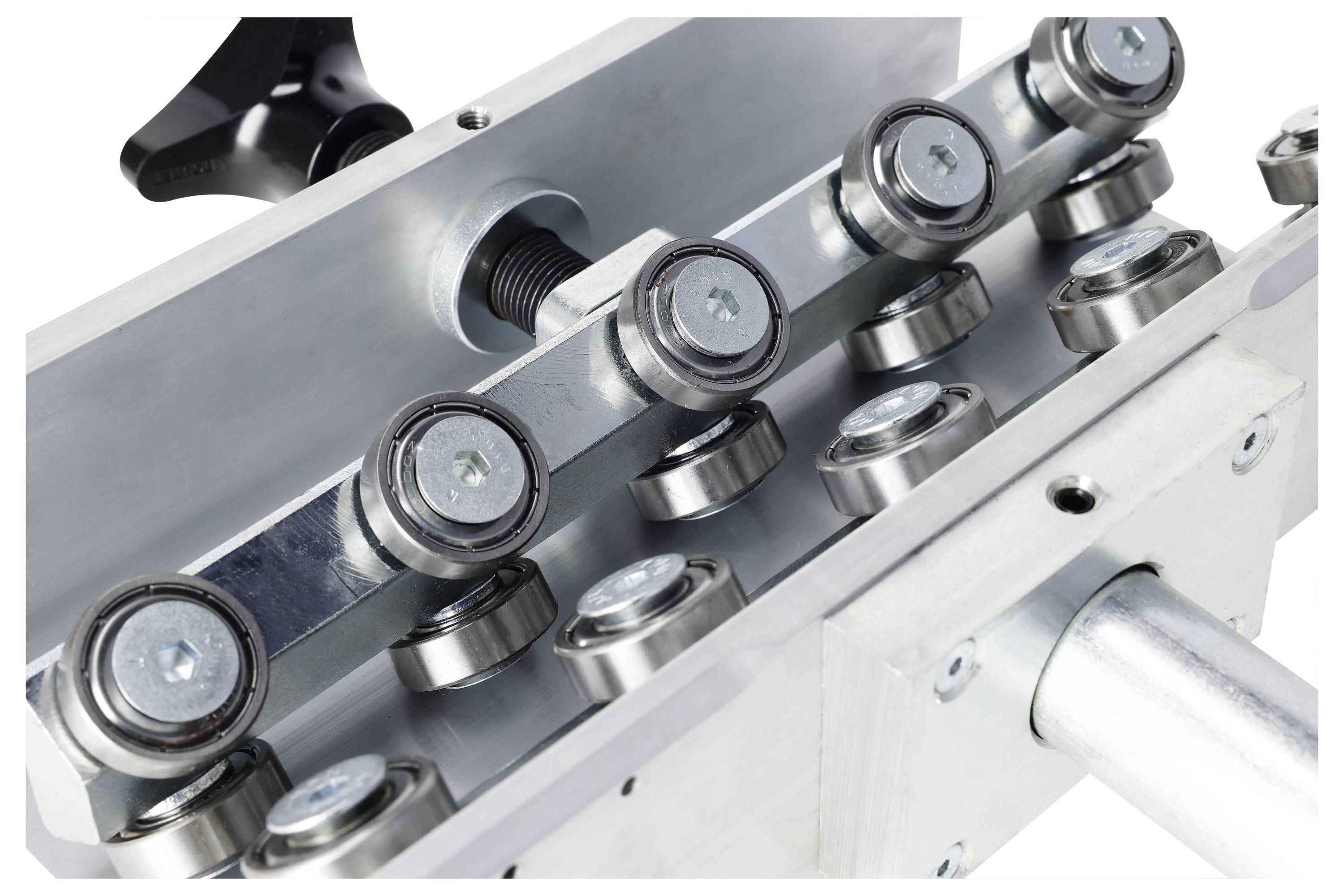 Close-up of a metal roller mechanism with multiple wheels and an adjustable screw, used for guiding or aligning materials in an industrial setting.