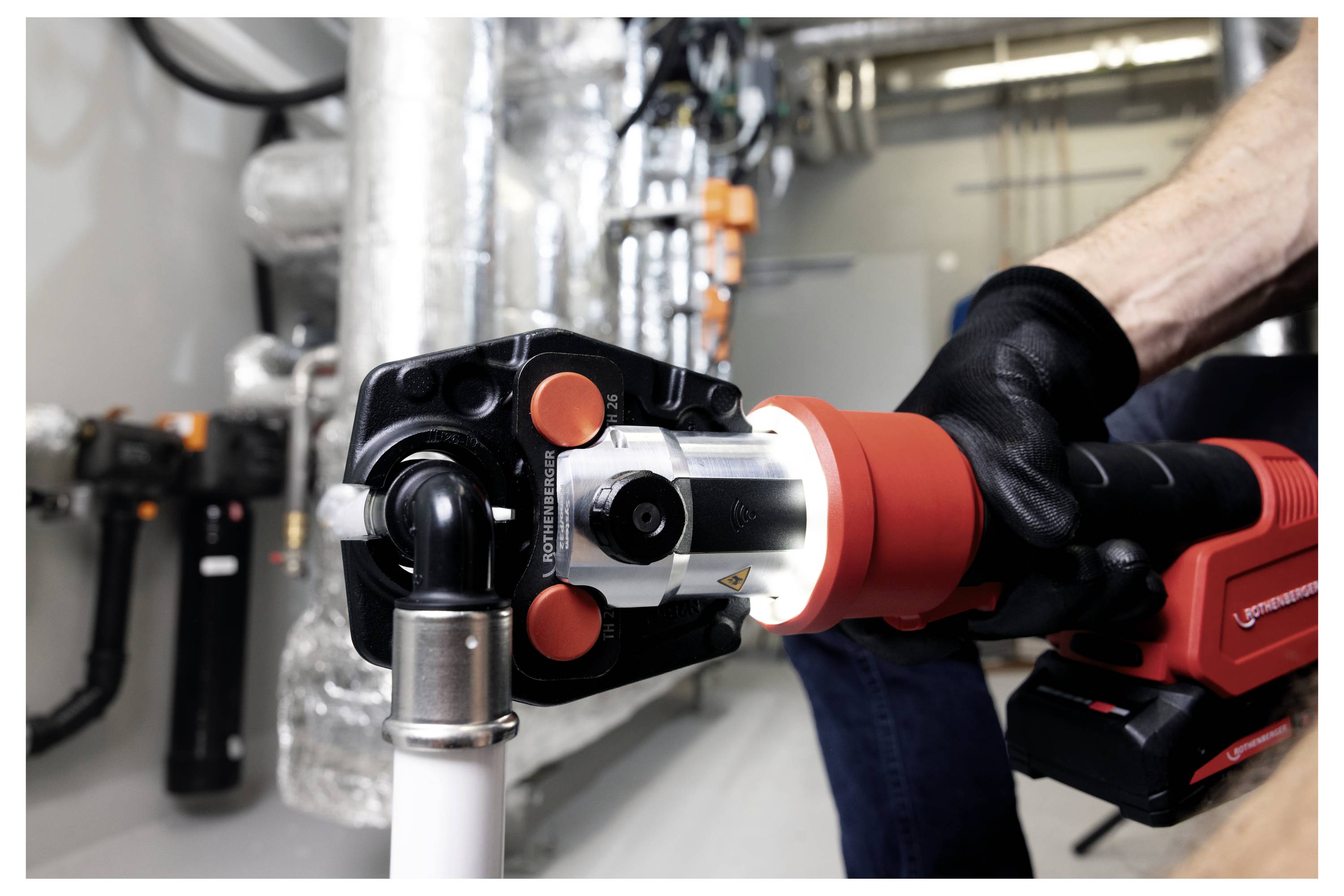 A person uses a hydraulic press tool on a pipeline in an industrial setting, showcasing tool operation and maintenance environment.