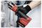 A gloved hand holds a red and black pipe press tool, pressing a plumbing pipe joint in an industrial setting.
