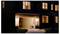 A two-story house with lit windows at night. The open garage reveals a robotic lawn mower parked inside, suggesting a secure storage spot.