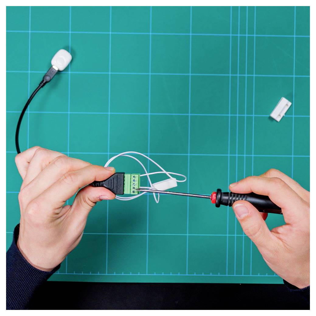 Hands shown assembling an electronic connector on a cutting mat with tools, indicating a work in progress on electronic components.