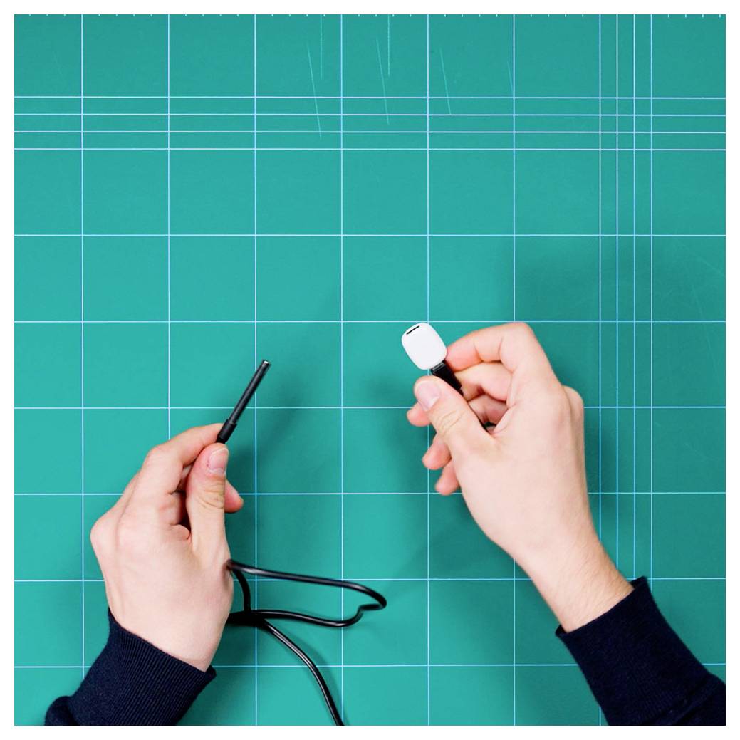 'A person is holding a soldering iron and a USB cable, appearing to be in the process of soldering or repairing it, over a green grid mat.'