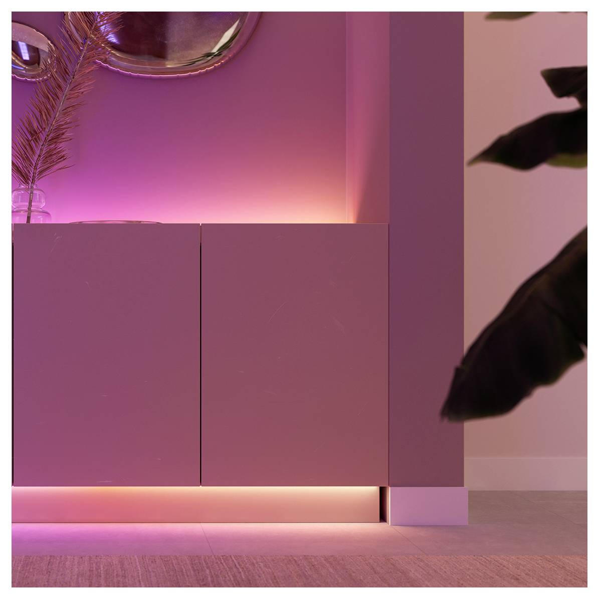 Warmly lit corner of a room with a soft pink glow beneath a modern cabinet and artistic wall decor, creating a cozy ambiance.