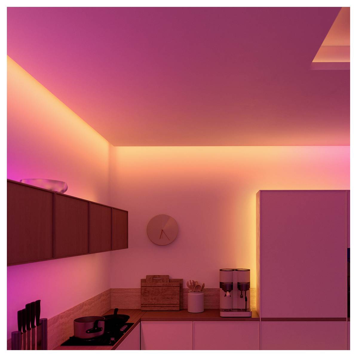 A modern kitchen illuminated with pink and orange LED lights, featuring a stovetop, knives, a clock, and a coffee maker on the counter.