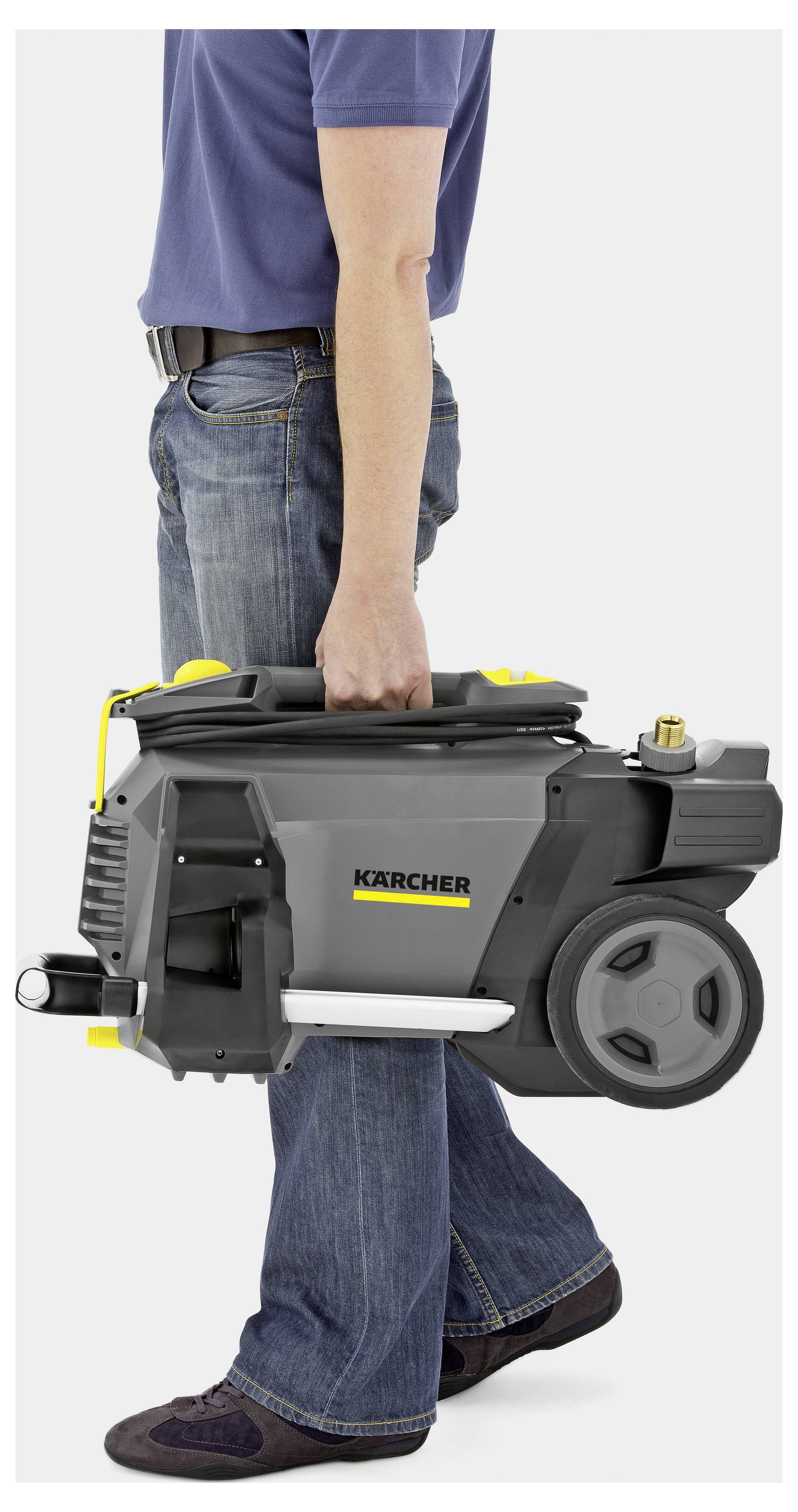 A person in jeans and a blue shirt carries a compact Kärcher pressure washer, showing its portability and ease of transport.