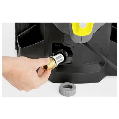A hand inserts a hose connector into a pressure washer, highlighting the connection process. A gray nozzle sits on the ground nearby.