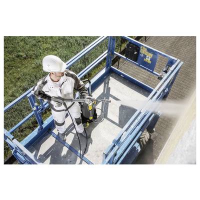 A person in safety gear operates a pressure washer on an elevated platform, directing the spray towards a large wall while ensuring stability.