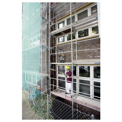 A person in a yellow hard hat stands on scaffolding next to a brick building, indicating construction or maintenance work in progress.