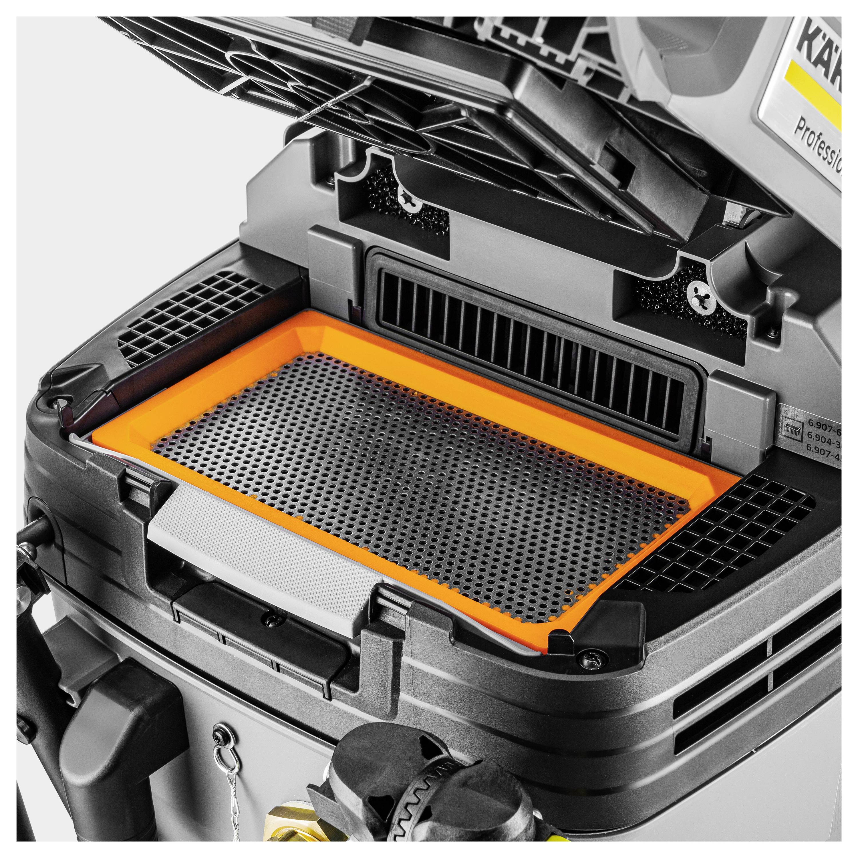 A close-up of a gray and orange air filter in a mechanical device, showing the rectangular filter housing with grid pattern and open cover.