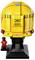 A detailed LEGO model of a yellow HP-sponsored racing helmet with a mini figure in a matching racing suit standing next to it.