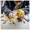 A person assembles a yellow LEGO globe on a table, surrounded by LEGO pieces and a red mini-figure, indicating a building activity.
