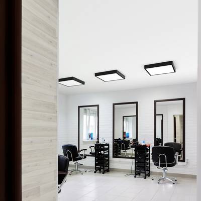 A modern hair salon interior with three styling stations, each featuring a large mirror, chair, and trolley, under bright ceiling lights.
