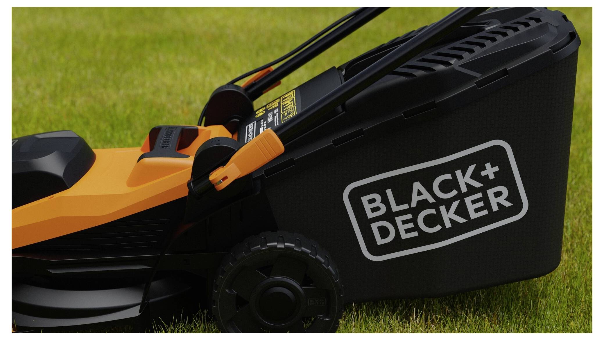 A close-up of a Black+Decker lawn mower on a green grass lawn, showing the side of the mower with its brand name on the grass collection bag.
