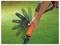 A hand adjusts the angle of a BLACK+DECKER lawn tool with an orange handle and multiple blade positions, set against a green lawn.