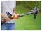 A person adjusts the length of an orange and black string trimmer in a grassy backyard, preparing it for use.