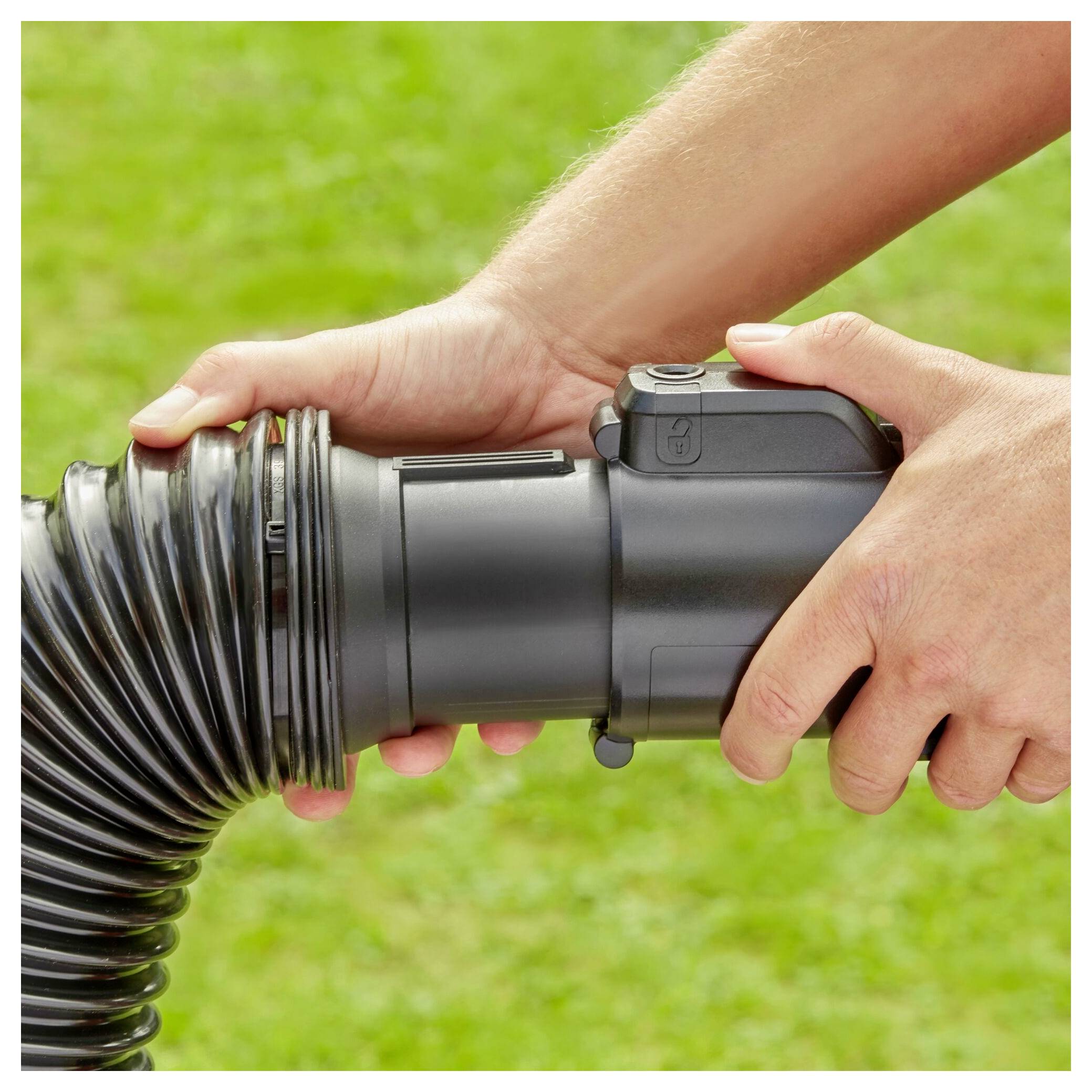 Hands connect a black corrugated drain pipe to a garden hose fitting, set against a blurred grassy background.