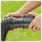 Hands connect a black corrugated drain pipe to a garden hose fitting, set against a blurred grassy background.