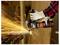 A person wearing gloves uses an angle grinder to cut metal, creating bright sparks that shoot outward.