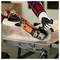 A person wearing gloves uses an orange and black cordless angle grinder to cut a piece of wood on a workbench, demonstrating carpentry skills.