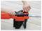 'A person adjusting the chain tension of an orange electric chainsaw using a tensioning knob located on the side of the tool.'